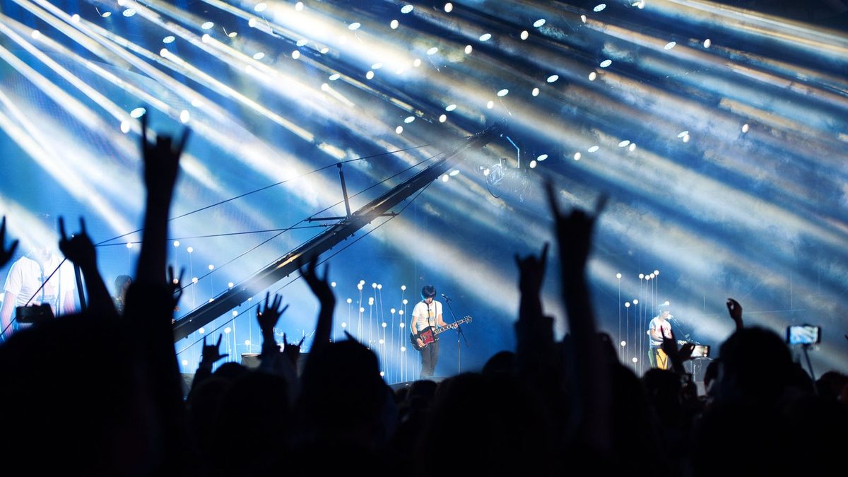 Público con las manos en alto bajo los focos azules de un concierto
